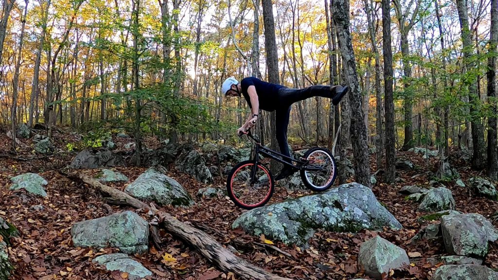 Tim balances atop a rock on his trials bike with one leg extended horizontally as a temporary counterbalance