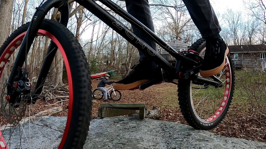 Tim on his trials bike atop a boulder with Dan watching in the background