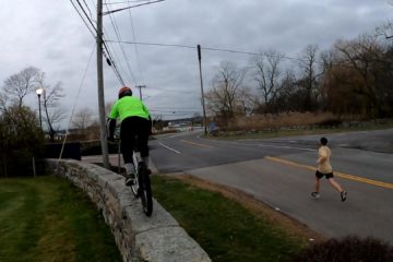 Scott rides his trials bike across a wall while a runner passes by