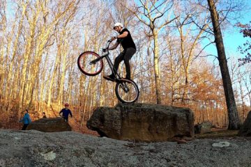 Tim on his trials bike rear wheel about to drop off a boulder while people walk by in the background