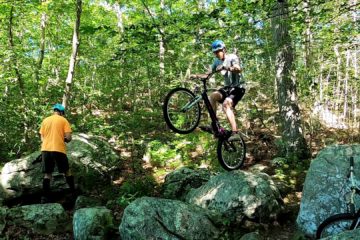 Alex balances on his trials bike's rear wheel, about to hop off a rock