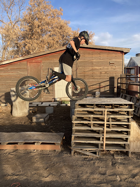 Bike trials hop up to front wheel on a tall stack of wooden pallets