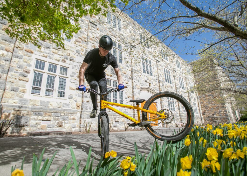 Nathaniel Moore does a footjam whip in front of a stone building with daffodils in the foreground